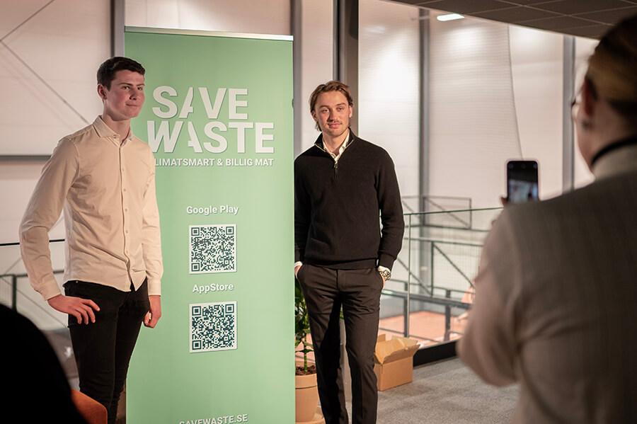 Malcolm och Victor vid en poster om appen Savewaste